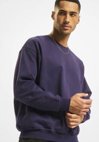 Sweatshirt purpuriu din material moale, cu guler rotund, mâneci lungi și manșete ribbate. Textură netedă, cu o croială lejeră.