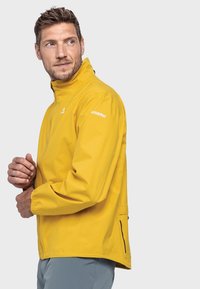 Gelbe wasserdichte Jacke mit hohem Kragen, Reißverschluss vorne, elastischen Bündchen und Logodetail an der Schulter. Leicht und mit glatter Textur.