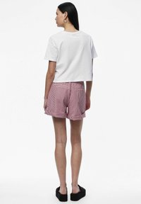 T-shirt bianco corto, pantaloni shorts a righe rosse e bianche, e sandali con platform neri. Tasche posteriori visibili sui pantaloni, texture in cotone liscia.