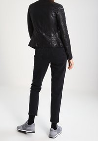 Černá kožená bunda s texturovanými detaily na ramenou a rukávech, v kombinaci s černými zúženými kalhotami a šedými teniskami. Měkký povrch, minimalistický profil.