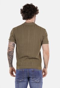 Polo a maniche corte in maglia verde oliva con texture a coste verticali e colletto classico, abbinato a jeans blu di denim.