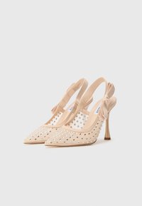 Talons beiges à bride arrière avec pointe effilée, panneaux en maille, ornés de strass, et un petit nœud décoratif sur le talon.