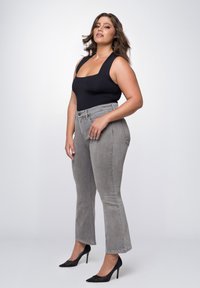 Zwarte aansluitende bodysuit, grijze high-waisted jeans met rechte pijpen en zwarte puntige hakken. Glad materiaal, minimalistisch ontwerp.