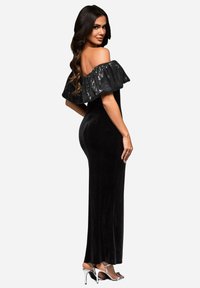 Mustat samettiset off-shoulder mekko, jossa on paljetilla koristeltu röyhelökaulus, vartalonmyötäinen silhouette ja lattiaa hipova pituus. Mukana strasseilla koristellut hopeiset korkokengät.