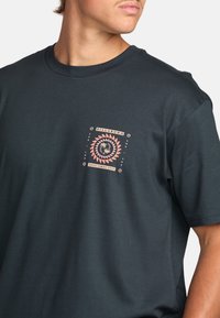 T-shirt noir à manches courtes en mélange de coton, avec un graphique sur le devant présentant des motifs de soleil et de vague en rose et blanc, centré dans un design bordé.