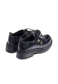 Zapatos de cuero negro con puntera redonda, suela de goma plana y banda de rodadura gruesa. Presentan cordones y ojales en tono dorado. Textura suave.