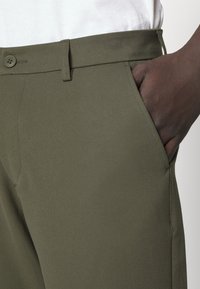 Olivgrüne Hosen aus strukturiertem Stoff, mit flachem Vorderteil, seitlichen Taschen und klassischem Knopfverschluss. Taillierte Passform, minimalistisches Design.