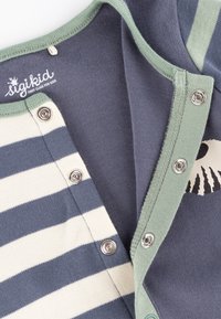 Gestreifter Baumwoll-Overall in Marineblau und Creme, mit einer grünen Druckknopfleiste und einem grafischen Muster. Weiche Textur und lässiges Design.