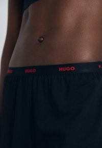 Sorte boksershorts laget av myk bomull med elastisk midje som har rød "HUGO" tekst. Jevn tekstur, ledig passform.