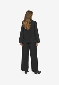 Cămașă neagră cu mâneci lungi dintr-un material moale, cu croială lejeră și cusături vizibile, asortată cu pantaloni negri cu picioare largi și cizme cu toc.