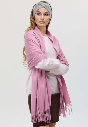 Sciarpa di cashmere rosa con orli frangiati, indossata sopra un maglione chiaro e una gonna scura. Un cerchietto grigio completa il look, aggiungendo texture.
