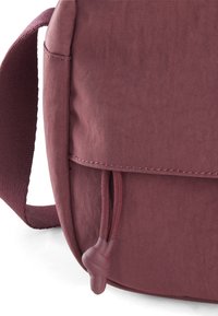 Piccolo borsetto di tessuto color bordeaux con una superficie texturizzata, dotato di chiusura a pattina e dettaglio con cordoncino. La tracolla è intrecciata e robusta.