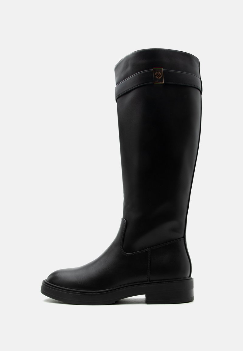 Botte haute en cuir noir avec un talon bas et une sangle décorative avec un emblème en métal près du haut, vue de profil sur fond blanc.