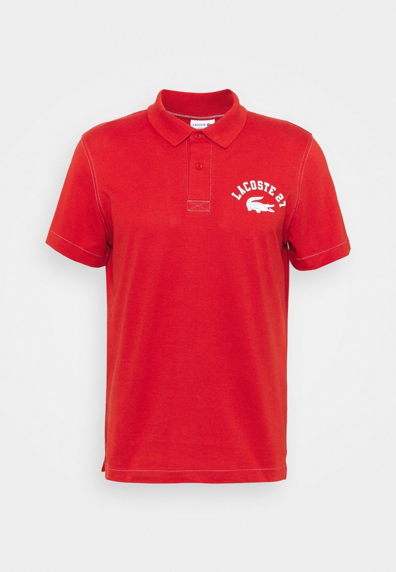 Polo rouge en coton doux, avec un col classique, une patte de boutonnage à deux boutons, et un logo brodé blanc sur la poitrine.