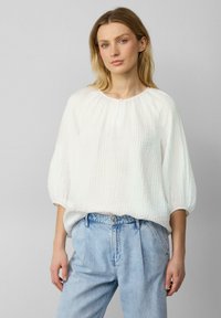 Witte textuur blouse met een ronde halslijn en een knopen detail aan de voorkant, gecombineerd met hoge lichtblauwe denim jeans.