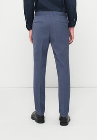 Ραμμένες ναυτικές παντελόνες με λεία υφή, διαθέτοντας δύο πίσω τσέπες και επίπεδο μπροστινό μέρος, σε συνδυασμό με μαύρα υποδήματα.