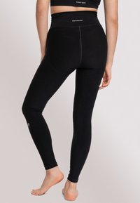 Leggings neri a vita alta realizzati in un tessuto elasticizzato, caratterizzati da una texture liscia e un piccolo logo vicino alla caviglia.