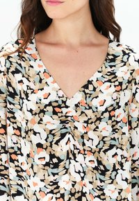 Blusa floreale con sfondo nero e motivi astratti multicolore, scollatura a V e dettagli arricciati al centro.