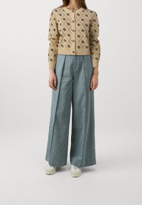 Cárdigan de punto beige con patrones geométricos negros y botones, combinado con pantalones anchos de color azul claro y zapatillas blancas.