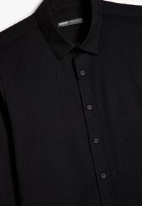 Camicia nera con bottoni, realizzata in tessuto testurizzato. Presenta un colletto classico e sei bottoni neri lungo la parte anteriore. Design a vestibilità regolare.