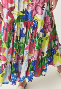 Vestido maxi floral que presenta una mezcla de colores vibrantes: rosa, azul, verde y rojo, con un dobladillo de volantes en capas y una textura de tela ligera.