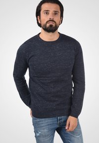 Sötétkék, textúrált pulóver, kerek nyakú fazonban, kötött anyagból készült, világoskék, kopott farmernadrággal párosítva.
