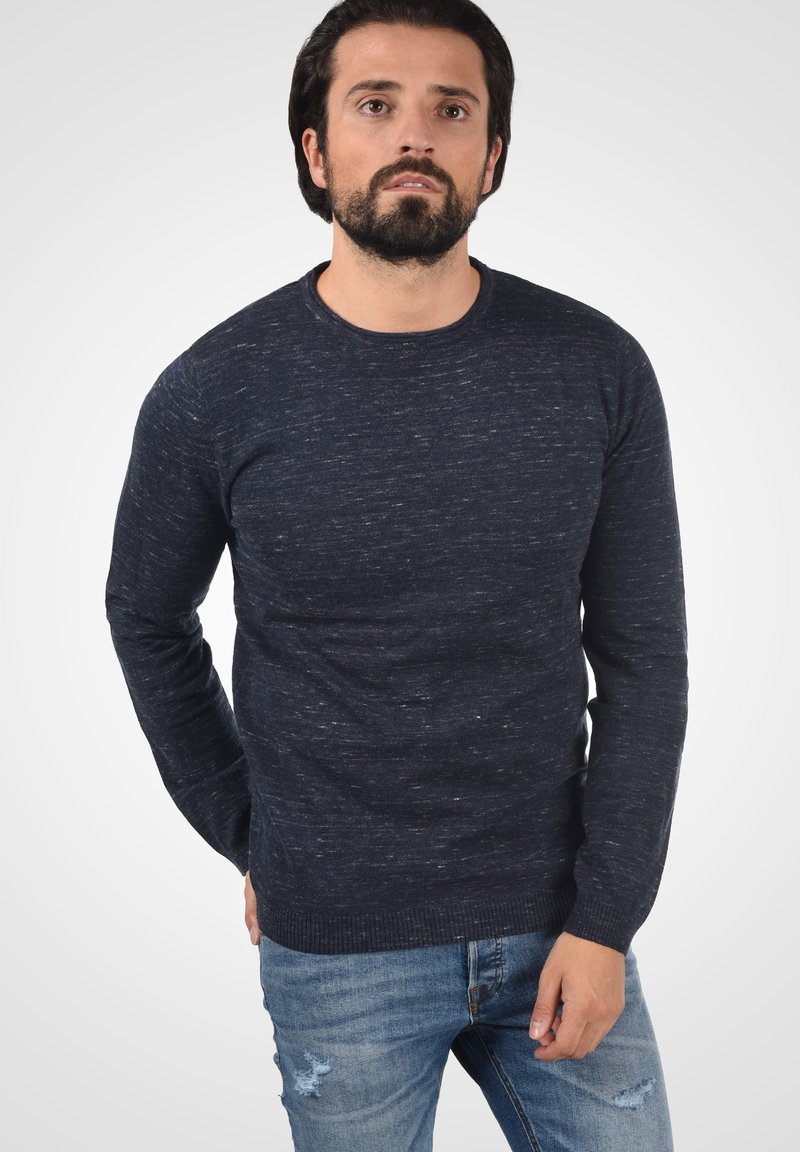 Marineblauwe, gestructureerde trui in een ronde hals design, gemaakt van gebreid materiaal, gecombineerd met lichtblauwe versleten jeans.