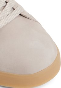 Sneaker beige chiaro con tomaia in suede liscio, lacci piatti intrecciati e suola in gomma a contrasto. La punta è arrotondata con una finitura testurizzata.