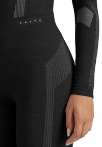 Chemise noire à manches longues en tissu tricoté texturé, arborant des rayures grises et un logo. Design ajusté qui met en valeur la silhouette et la texture.