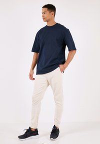 Tengerészkék, oversized póló, rövid ujjú, krémszínű jogger nadrágokkal és fekete sportcipőkkel párosítva. Simaszerkezetű anyag, laza szabás és rugalmas mandzsetták.