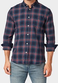 Camicia a quadri blu navy con controlli rossi e azzurri, maniche lunghe arrotolate fino ai gomiti e una tasca sul petto. Materiale in cotone.
