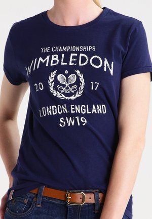 Osoba nosząca granatowy t-shirt z białym napisem i grafiką rakiety tenisowej z napisem Wimbledon Championships 2017 London England SW19.