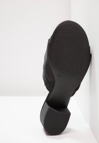 Semelle d'une chaussure à talon noire avec un motif de bande de roulement ressemblant à une empreinte digitale et la taille 37, sur une surface blanche.