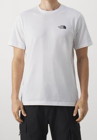 Camiseta de algodón blanca con un logo negro de The North Face en el lado izquierdo del pecho, con cuello redondo clásico y mangas cortas.