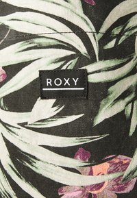 Plátená taška s tmavým pozadím, na ktorom sú zelené palmové listy a ružové kvety; obsahuje čiernu nášivku "ROXY".