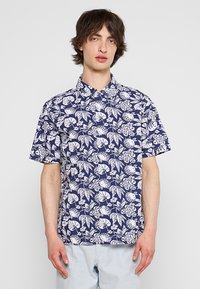 Maglietta a maniche corte in tessuto blu navy, con motivo floreale e foglie bianche, colletto classico e vestibilità ampia.
