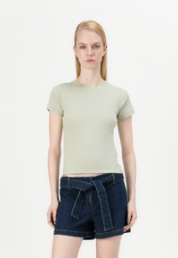 Light green fitted t-shirt with short sleeves, paired with dark denim shorts featuring a tied belt and large front pockets.