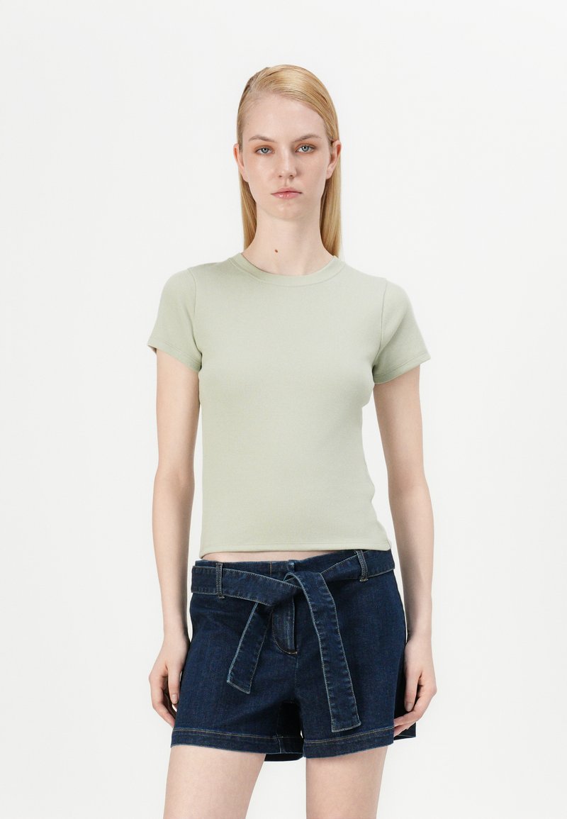 Ljust grönt figursytt t-shirt med korta ärmar, kombinerat med mörka jeansshorts med knytbälte och stora framfickor.