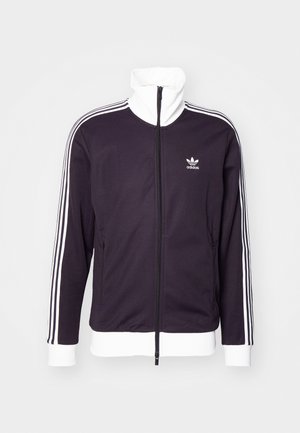 Veste noire zippée avec col et poignets blancs, ornée de trois bandes blanches le long des épaules et du logo Adidas sur la poitrine.