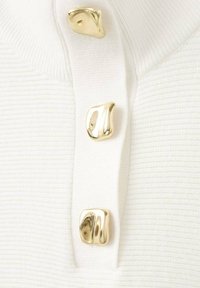 Tissu blanc côtelé avec trois boutons dorés brillants de forme irrégulière, disposés verticalement le long d'une patte de boutonnage.