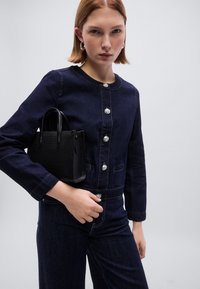 Μπλε τζιν μπουφάν με ασημένια κουμπιά, σε συνδυασμό με μια μικρή μαύρη τσάντα με υφή. Διαθέτει εφαρμοστή σχεδίαση και ομαλές ραφές σε αντίθεση.