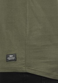 Olijfgroene katoenen T-shirt met een rechte snit en afgeronde zoom; voorzien van een zwart label met de tekst "ISOLID" nabij de onderkant.