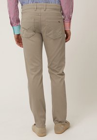 Pantalones de algodón beige con corte recto, que incluyen bolsillos traseros en ángulo y detalles de costura sutiles. Llevados con calzado de color claro.