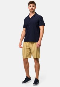 Chemise à manches courtes navy, associée à un short à rayures jaunes, portée avec des baskets noires. Design décontracté, tissu léger.