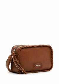 Wristlet in pelle marrone con bordi intrecciati, borchie argentate e chiusura a zip. Dotato di una tracolla rimovibile e un'etichetta con logo. Forma rettangolare e compatta.