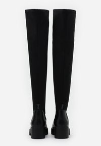 Černé kozačky po kolena s robustními podpatky, hladkým koženým povrchem na noze a pružnou látkovou holeně, zobrazené zezadu na bílém pozadí.