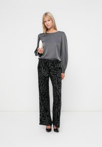 Grå satinbluse med puffærmer, parret med sorte mønstrede brede bukser med en diskret zebra-lignende design og metalliske detaljer.