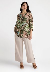 Blusenhemd mit floralem Muster in Grün, Rosa und Creme; lockerer Schnitt. Kombiniert mit beigen, weit geschnittenen Hosen und braunen Plateausandalen.
