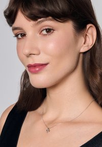 Srebrny naszyjnik z wisiorkiem w kształcie liścia na cienkim łańcuszku, noszony na szyi. Gładka tekstura i minimalistyczny styl.