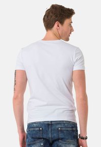 Weißes kurzärmeliges T-Shirt aus Baumwolle mit rundem Ausschnitt. Die Rückseite zeigt nahtloses Nähen und ein tailliertes Design. Getragen mit blauen Denim-Jeans.
